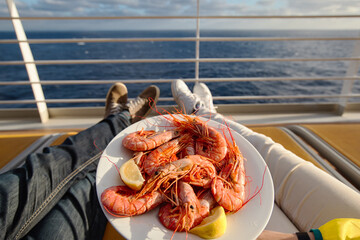 a young couple holds a plate with shrimps while on a cruise ship