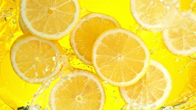 Super Slow Motion Shot of Lemon Slices Falling into Water on Yellow Background at 1000fps.