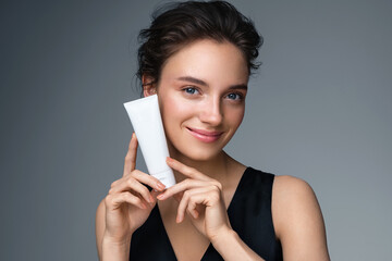 Woman holds tube with cosmetic cream. Photo of attractive woman with perfect makeup on gray...