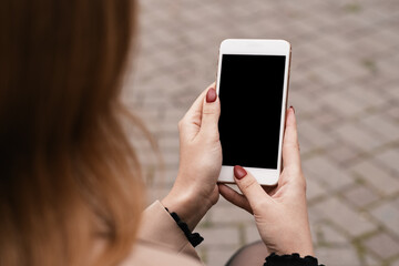 Cropped close up of woman hands holding and using mobile phone, smartphone with empty black screen in city park outdoors. Technology, communication concept