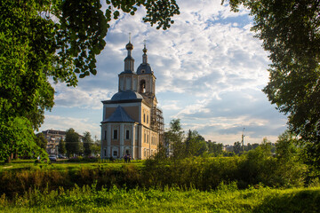 Fototapeta na wymiar yellow Church of the Kazan icon of the mother of God among green trees against a cloudy sky and space for copying in Uglich Russia
