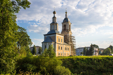 Fototapeta na wymiar yellow Church of the Kazan icon of the mother of God among green trees against a cloudy sky and space for copying in Uglich Russia