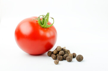 Closeup of one fresh tomato and black ppercorns on the white background
