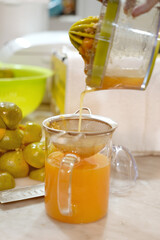 Freshly squeezed orange juice is being poured into the glass jug. Woman hand pouring squeezed orange juice from a juicer into a glass jar.
