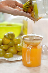 Freshly squeezed orange juice is being poured into the glass jug. Woman hand pouring squeezed orange juice from a juicer into a glass jar.