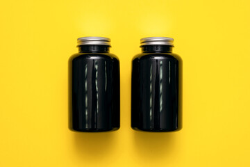 Black plastic jars on the yellow flat lay background.