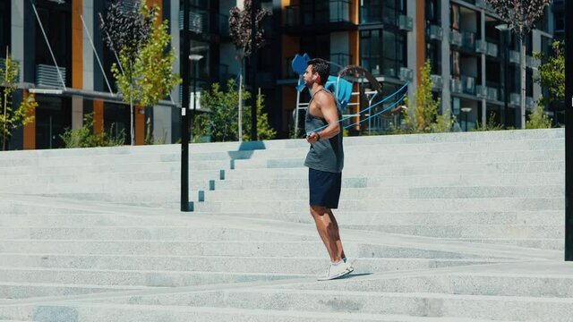 Young man exercising outside. Slow motion of sportsman in slow running or jogging on street exercising. Workout or training passing urban building apartments. Back view.