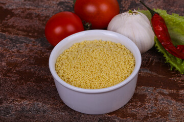 Raw couscous in the bowl served salad leaves, tomato and pepper