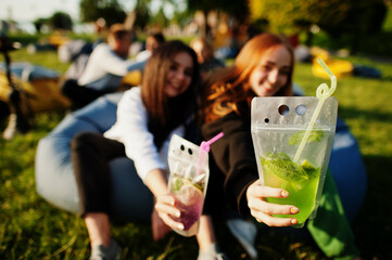 Young multi ethnic group of people watching movie at poof in open air cinema. Two girls with mojito...