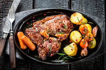Roasted steak with vegetables and herbs on burned table