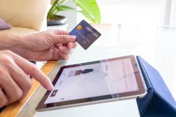 Selective focus at men hand pressing purchase button on digital tablet for online shopping with blurred credit card as background. Online payment concept to support social distance.