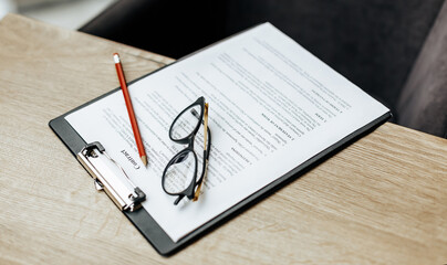 A contract on a wooden work table with glasses and a red pencil. The documents are ready for signing. Business concept. Collaboration agreement.