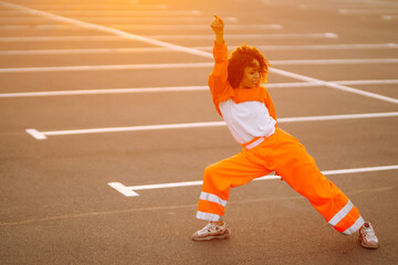 Obraz premium Stylish girl - dancer dancing in the street at sunset. Beautiful African American woman with curly hair in an orange suit. Sport, dancing and urban culture concept.