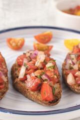 Mediterranean bruschetta with tomato, olive oil, parsley and red onion placed on a white background.