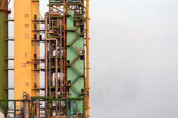 A close-up of a high industrial building of an ammonia plant, a tower with pipes and a ladder for servicing against the sky with copy space for text.