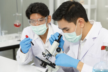 Two Male Scientists wear Face Mask working in Lab while Checking Blood tested by micro scope. SARS-CoV-2 , Covid-19 THEME.