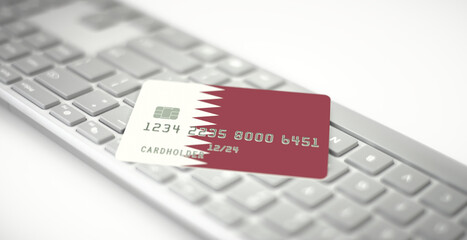 Plastic bank card depicting flag of Qatar on computer keyboard. Fictional numbers