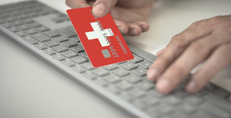 Man pays online with plastic bank card with printed flag of Switzerland. Fictional numbers