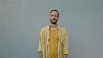 Front view portrait of handsome bearded man smiling and standing against a grey wall. Male expressing emotion