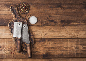 Vintage hatchets for meat on wooden chopping board with salt and pepper on wooden table background. Space for text