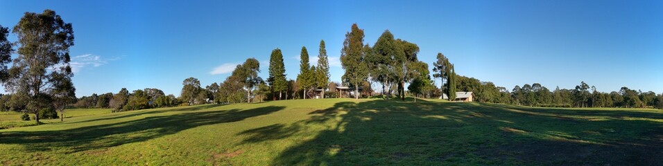 Fototapeta na wymiar Beautiful morning panoramic view of a park with green grass, tall trees and blue puffy sky, Fagan park, Galston, Sydney, New South Wales, Australia