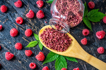 Freeze dried raspberries in a glass jar and a wooden spoon on a black background. Concept of berry storage types - obrazy, fototapety, plakaty