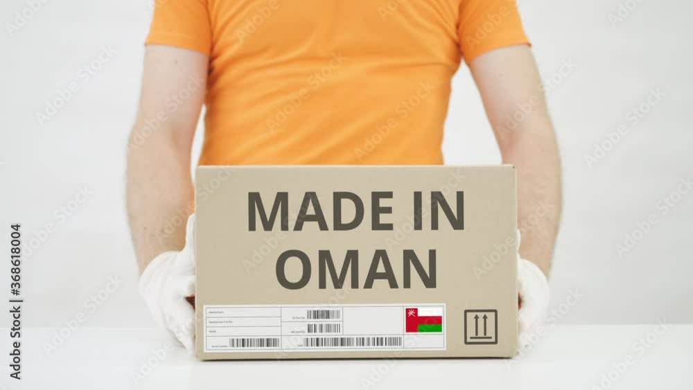 Poster worker wearing orange uniform puts box with made in oman print on the table