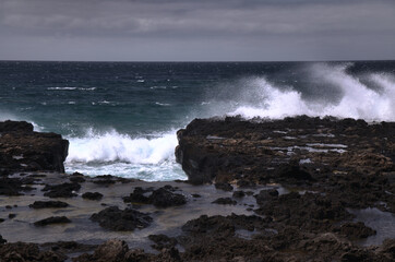 Gran Canaria, north west coast around natural swimming pools Salinas de Agaete, 
waves breaking against old eroded dark lava platform
