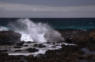 Gran Canaria, north west coast around natural swimming pools Salinas de Agaete, 
waves breaking against old eroded dark lava platform

