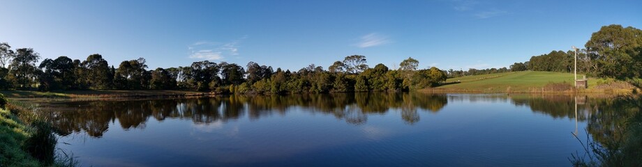 Fototapeta na wymiar Beautiful morning panoramic view of a peaceful pond in a park with reflections of deep blue sky and tall trees, Fagan park, Galston, Sydney, New South Wales, Australia