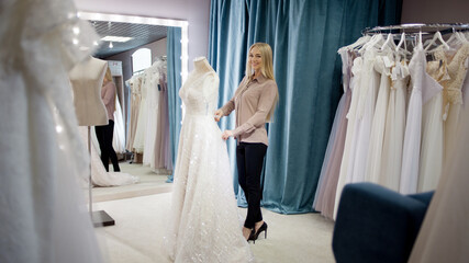 hostess of the wedding salon looks at the wedding dress. Small business,