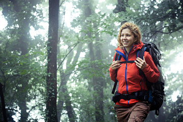 Smiling caucasian female backpacker, walking through misty forest.