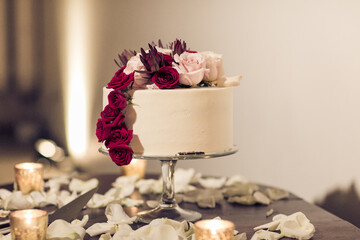 cream colored wedding cake with red and pink roses and copy space on table with rose petals
