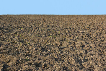 A rough stony field lies ploughed and cultivated ready for sowing spring crops, on a sunny hillside...