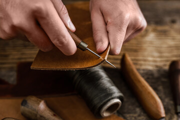 Close up of a shoemaker or artisan worker hands. Leather craft tools on old wood table. Leather...