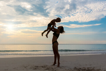 Mother with son are playing on a beach during sunrise time. Happy loving family concept. Summer time vacation.