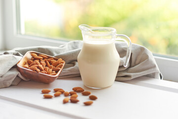 Almond milk in glass with almonds in wooden bowl on a white wooden table