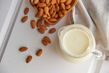 Almond milk in glass with almonds in wooden bowl on a white wooden table