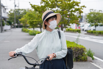 マスクを付けた中年女性。町中を自転車を押している