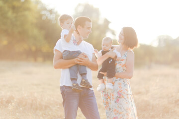 Family with children walking outdoors in summer field at sunset. Father, mother and two children sons having fun in summer field. People, family day and lifestyle concept