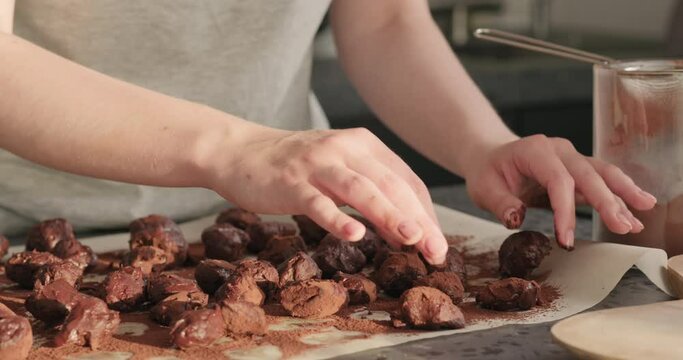 Slow motion handheld shot of young woman rolling chocolate truffles in cocoa powder on home kictchen