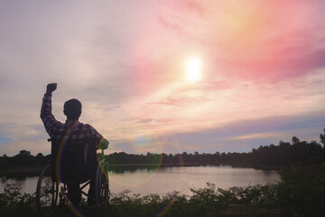 Fototapeta na wymiar Silhouette young disabled man seeing river background.He is raise a hand to and sitting on wheelchair.despair,lonely,hope.Photo concept depression and Patient.
