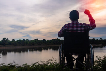 Silhouette young disabled man seeing river background.He is raise a hand to and sitting on wheelchair.despair,lonely,hope.Photo concept depression and Patient.