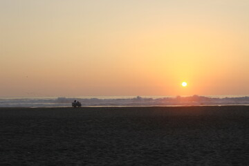 Puesta de sol en playa en Lima, Perú con pareja viendo  el atardecer desde lejos