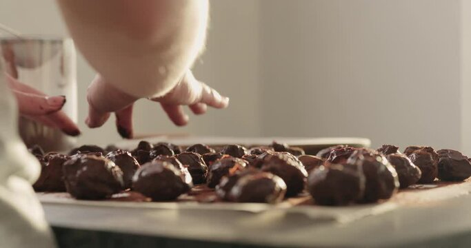 Slow motion handheld shot of young woman rolling chocolate truffles in cocoa powder on home kictchen