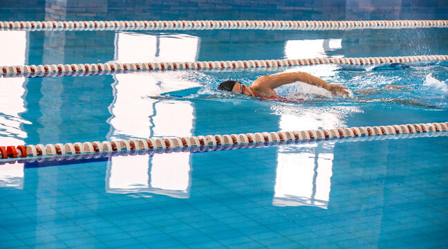 Young woman swimmer is swimming in the pool. Freestyle stroke, front crawl stroke. Swimming in blue pool, side view