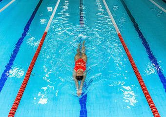 Woman swimmer swims backstroke in the pool. Top view, backstroke training