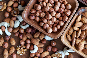 Wooden bowl with mixed nuts on table top view. Healthy food and snack. Walnut, pistachios, almonds, hazelnuts and cashews.