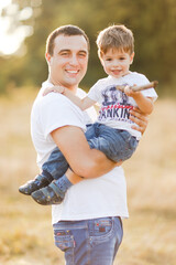 Fototapeta premium Family with children walking outdoors in summer field at sunset. Father and his little son having fun in summer field. People, family day and lifestyle concept