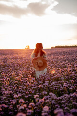 Beautiful young woman in a straw hat on a phacelia flower field at sunset